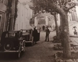 Foto en blanc i negre on veuen dos vehicles d'època amb uns clients arribant a l'antic Balneari de Cardó.